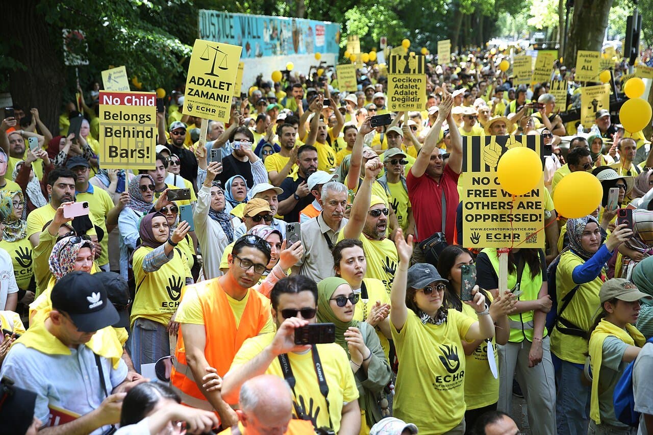 Foule en t-shirts jaunes brandissant des pancartes et des ballons jaunes à Strasbourg, devant le Mur de la justice.
